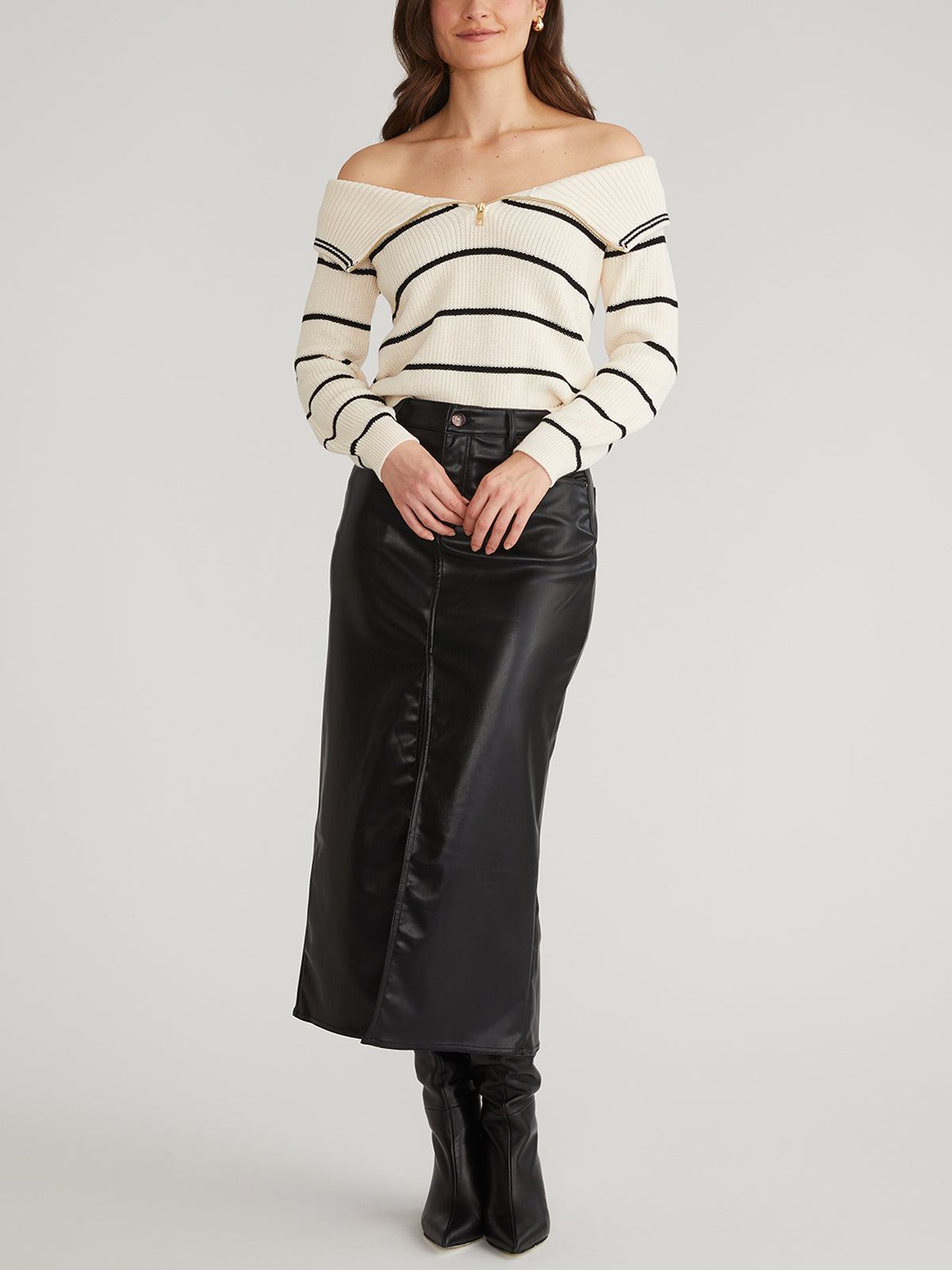 A person wears a 525 America striped pullover with an adjustable zippered neckline, paired with a long black leather skirt and black boots. They stand against a plain background, hands clasped in front.
