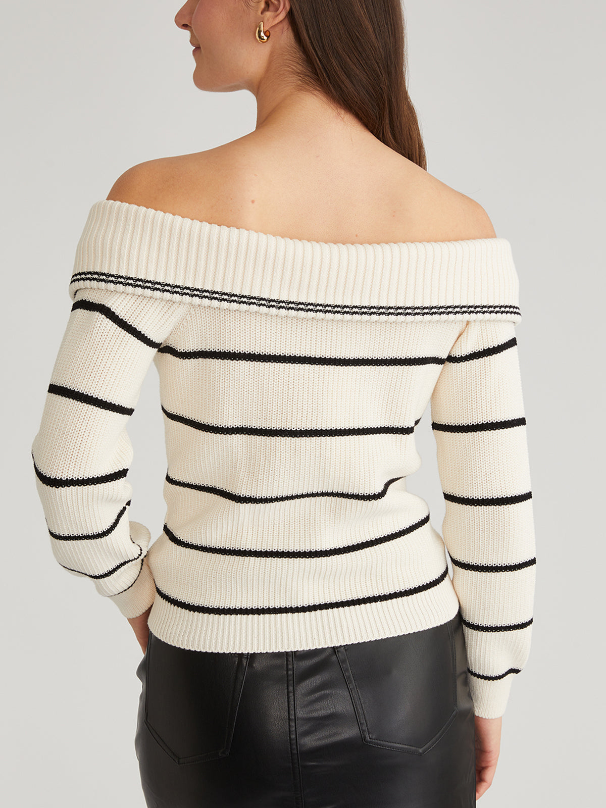 A person with long brown hair is seen from the back wearing a 525 America off-the-shoulder striped pullover featuring black horizontal stripes and a stylish adjustable zippered neckline. The 100% cotton sweater is paired with a black leather skirt.