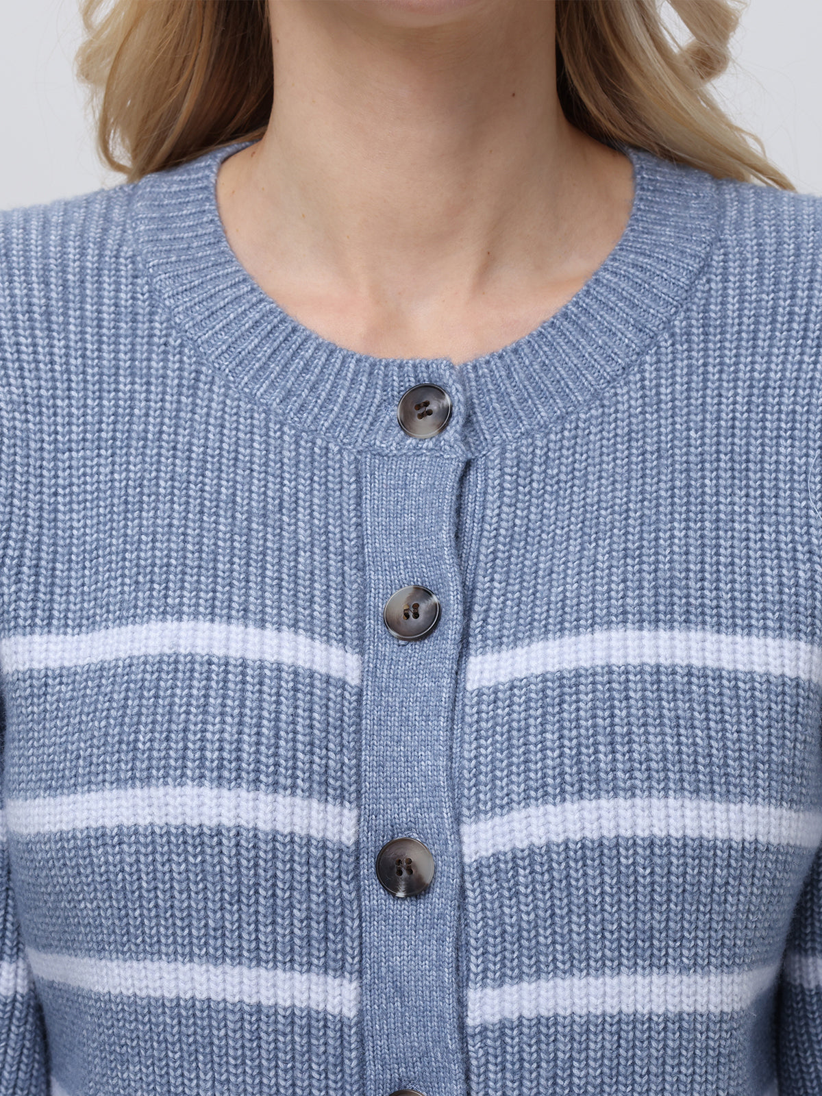 A person models a chic blue and white striped knitted cardigan from 525 America, featuring dark buttons, a round neckline, white horizontal stripes, and striking balloon sleeves. The photo emphasizes the upper body to showcase the garments intricate details.