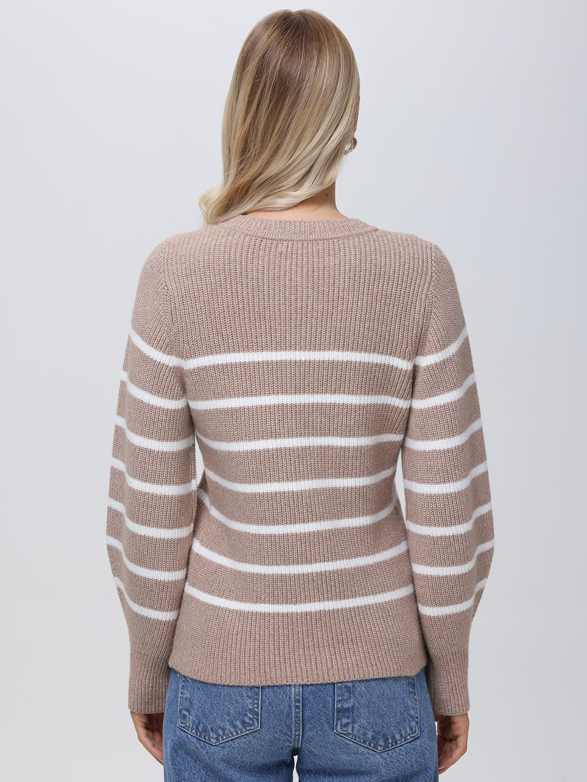 A person is shown from the back wearing a beige and white striped balloon-sleeve sweater by 525 America, paired with blue jeans. Their blonde hair falls in loose waves against a simple gray backdrop.