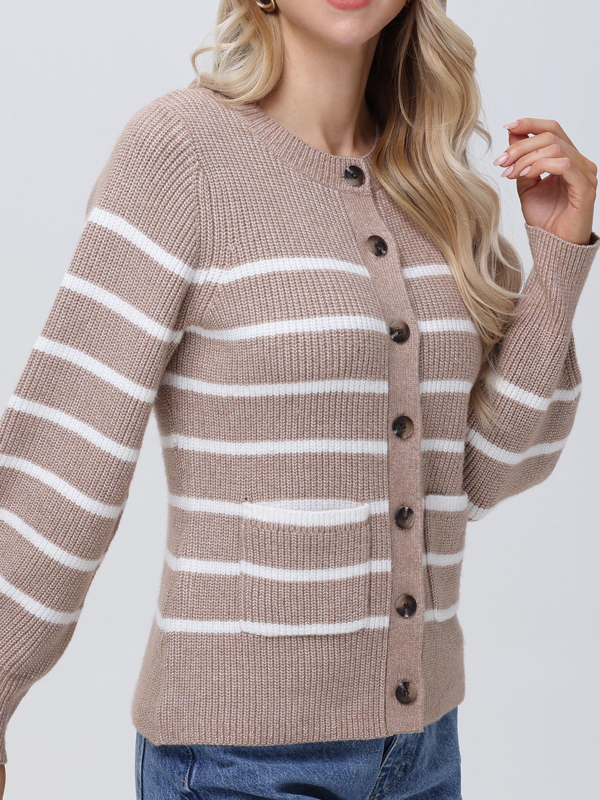 A person poses against a plain background, wearing blue jeans and a beige and white striped cardigan with balloon sleeves from 525 America. The cardigan features large buttons and a ribbed texture, complementing their long blonde hair.