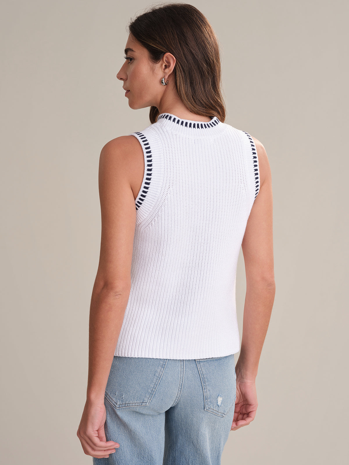 A person with straight brown hair is shown from the back, wearing a 525 America cotton sweater-tank with black and white striped trim at the armholes and collar, paired with light blue jeans.