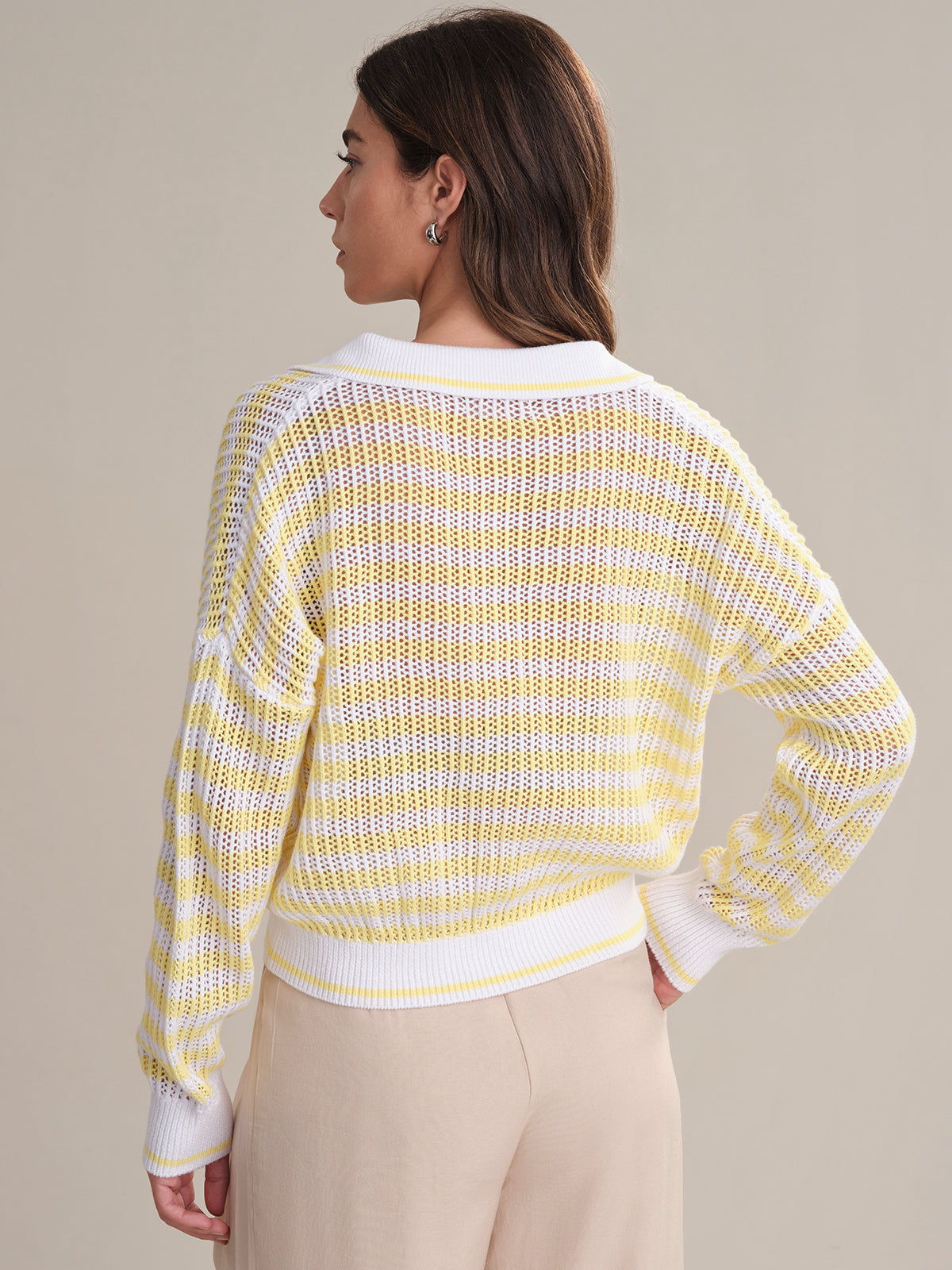 A woman faces away, wearing a 525 America yellow and white checkered 100% cotton polo sweater with white cuffs and collar, paired with light beige pants against a plain neutral background.