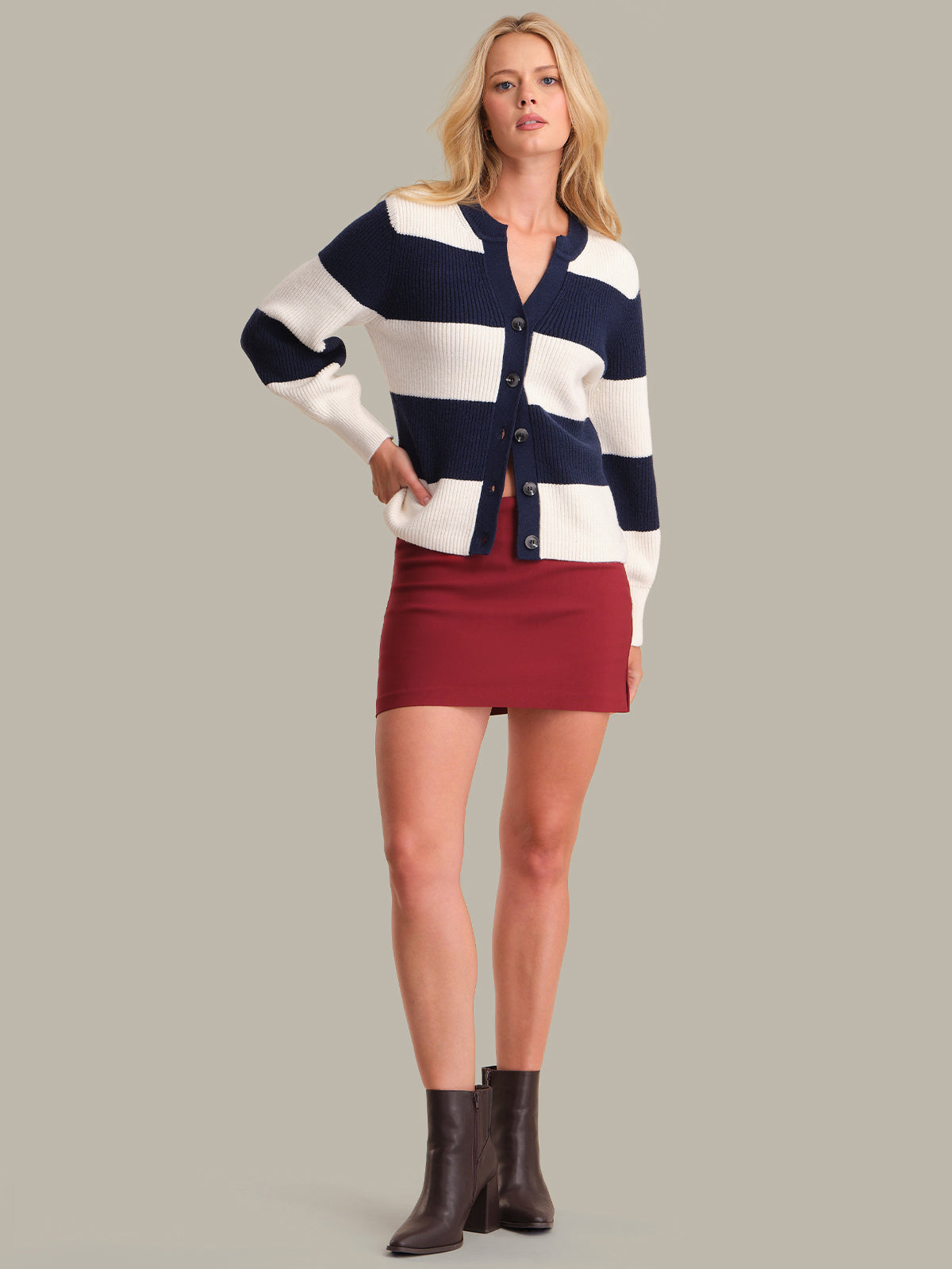 Woman wearing a striped cardigan, red skirt, and brown boots on a plain background