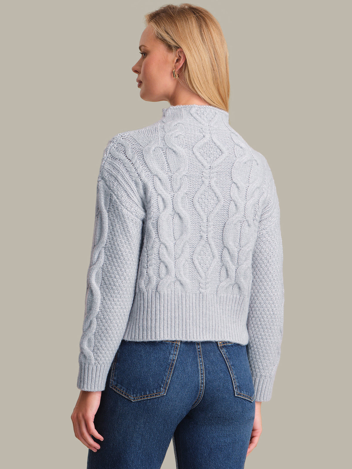 Woman wearing a light blue cable knit sweater and blue jeans on a beige background