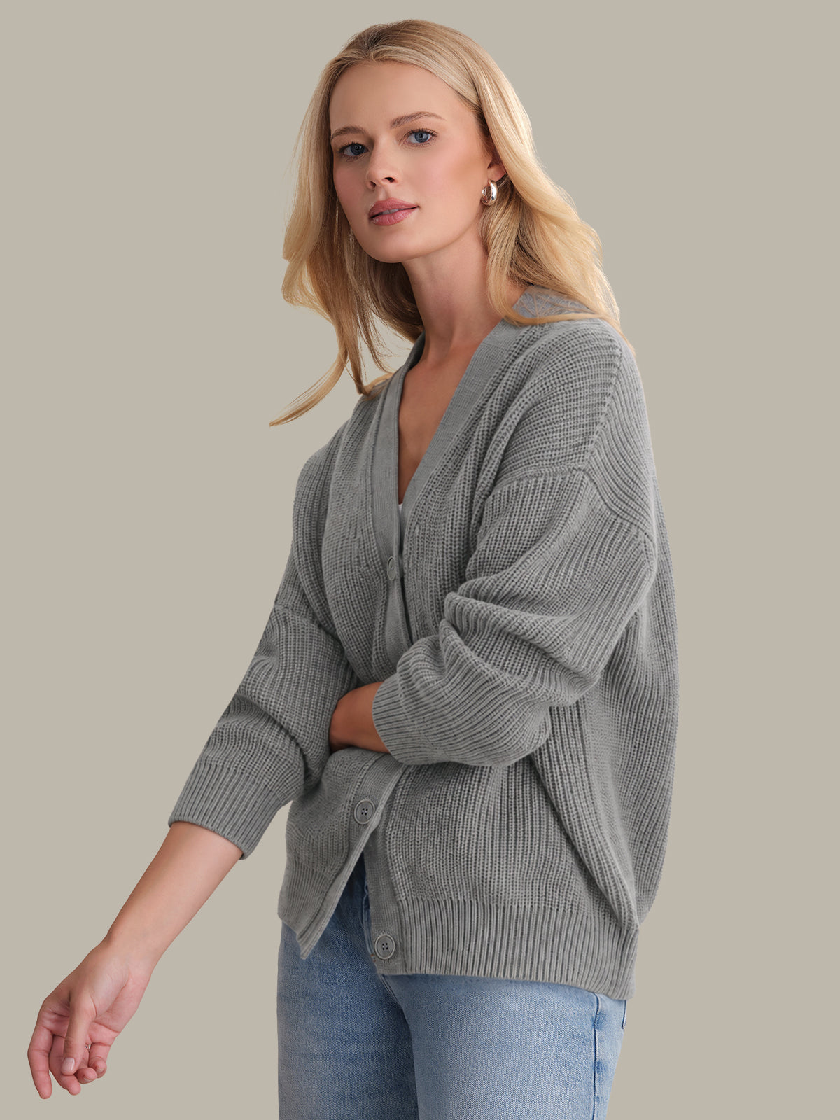 Woman wearing a gray sweater and blue jeans against a beige background