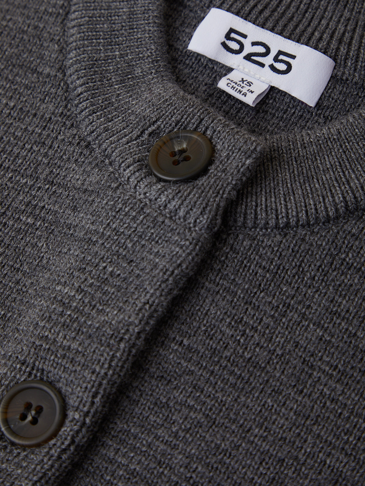 Close-up of a gray garment with a button and brand tag displaying '525'.