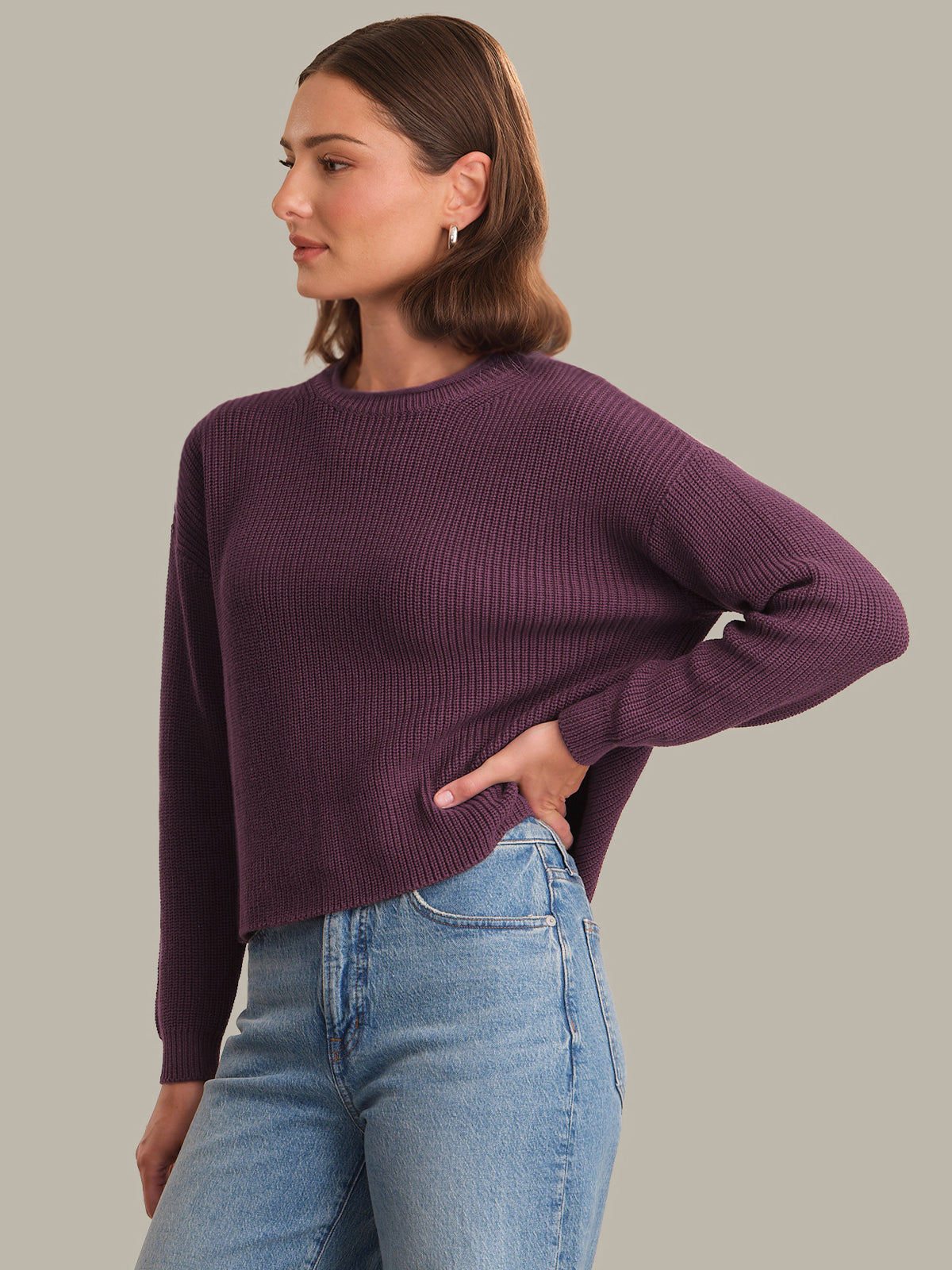 Woman wearing a purple sweater and blue jeans against a neutral background