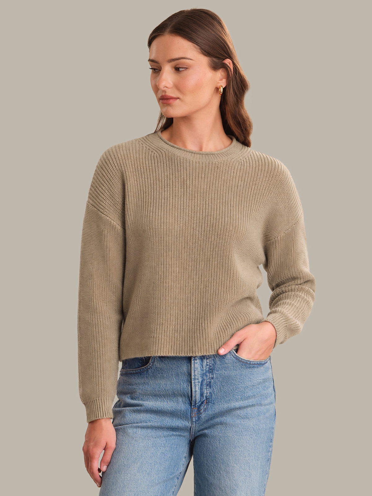Woman wearing a beige sweater and blue jeans against a gray background