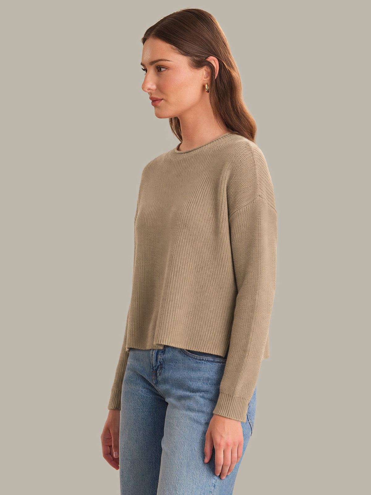 Woman wearing a beige sweater and blue jeans against a gray background