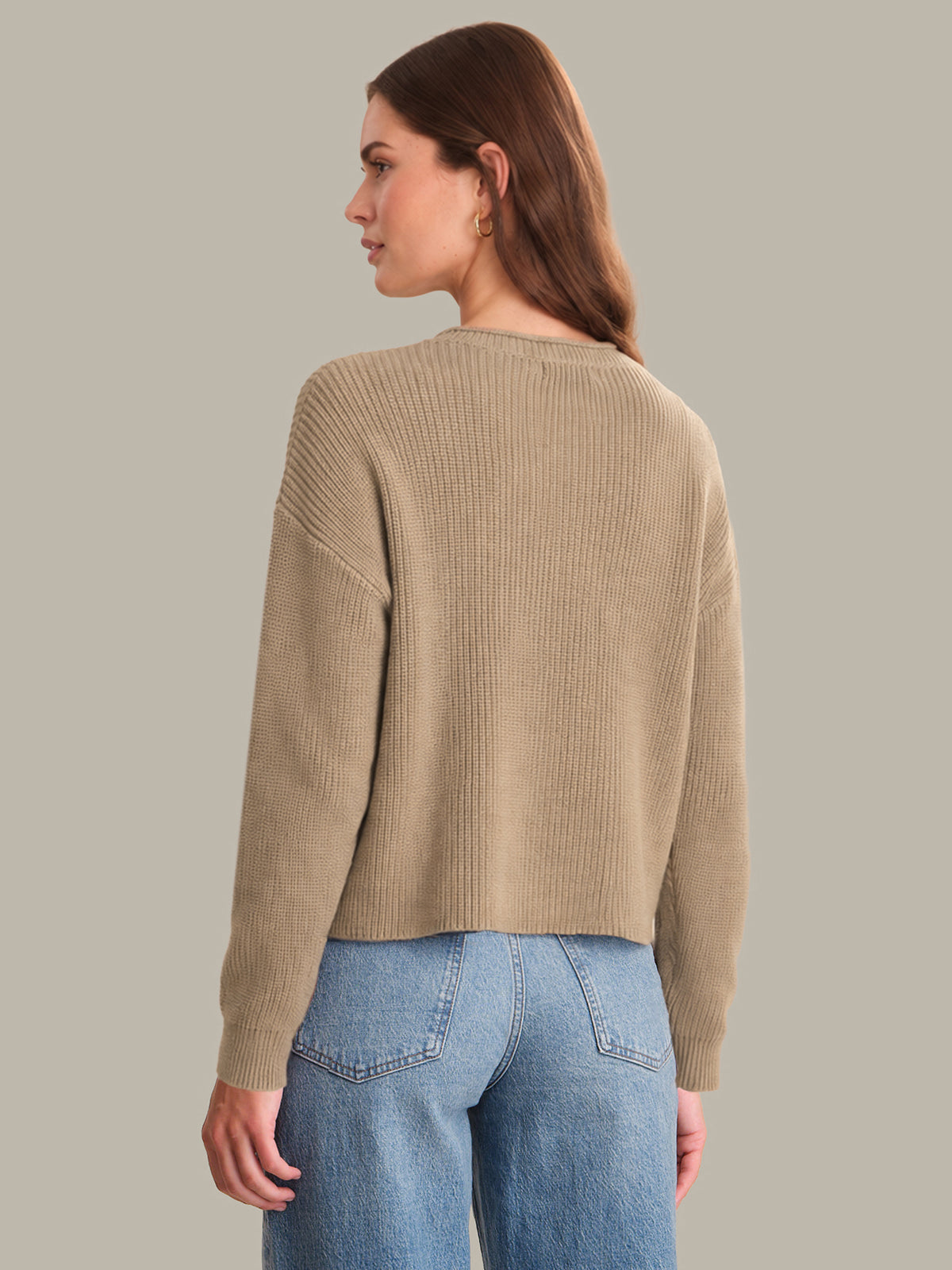 Woman wearing a beige sweater and blue jeans on a plain background