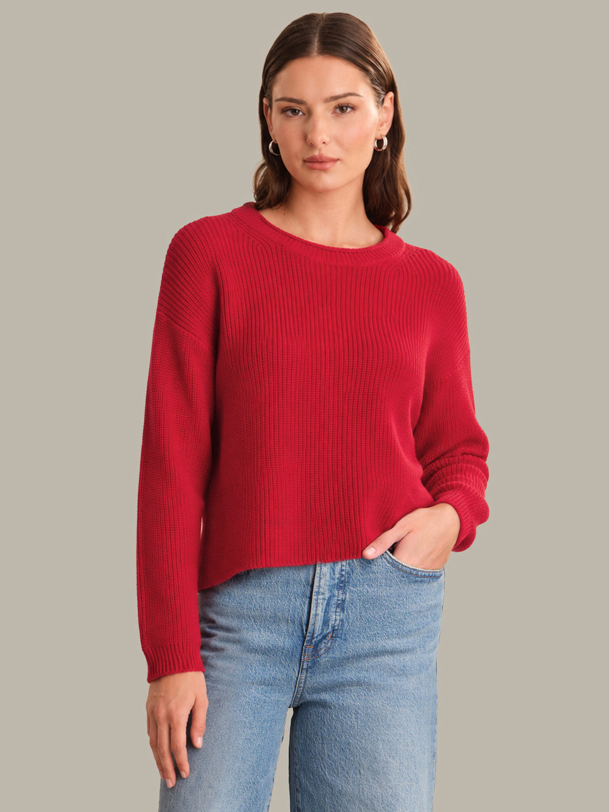 Woman wearing a red sweater and blue jeans against a gray background