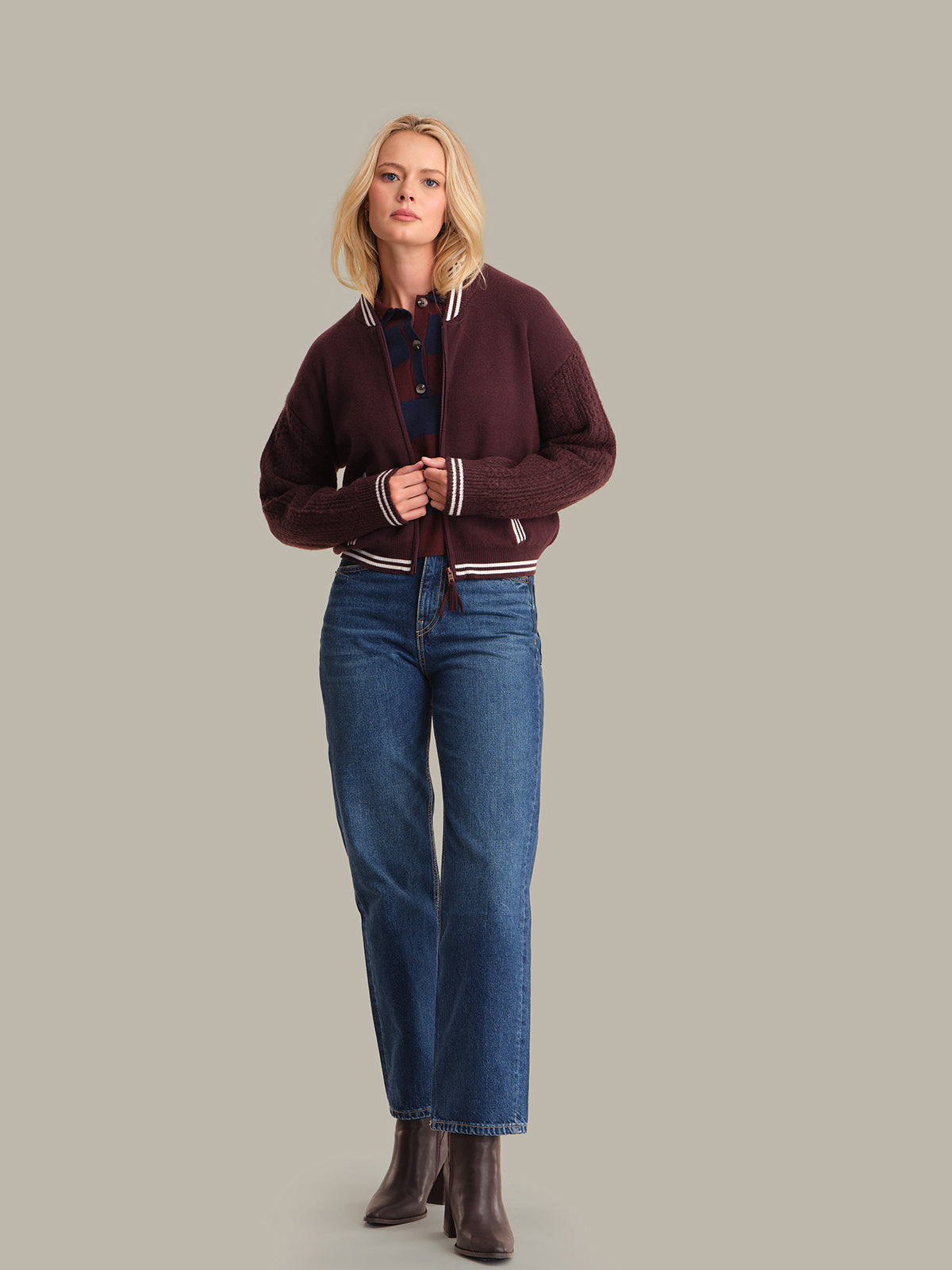 Woman wearing a maroon cardigan and blue jeans on a plain background