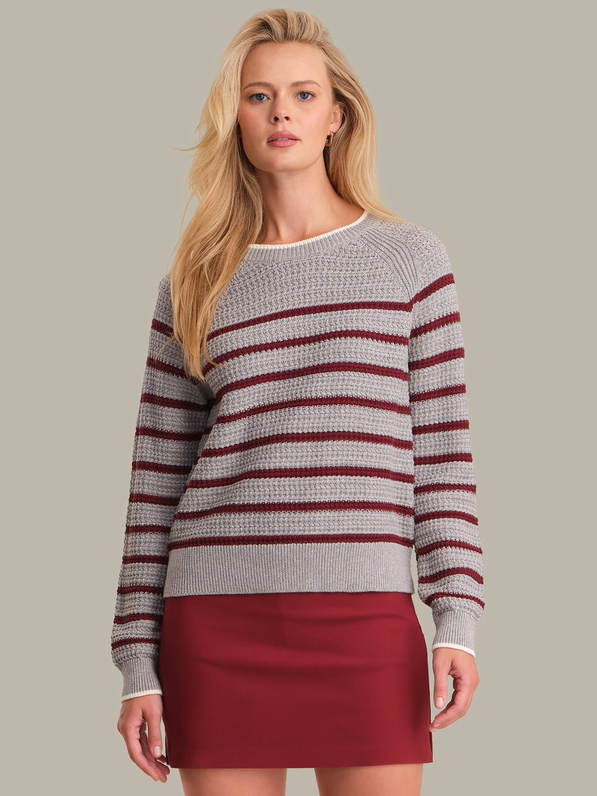 Woman wearing a gray and red striped sweater with a red skirt on a plain background