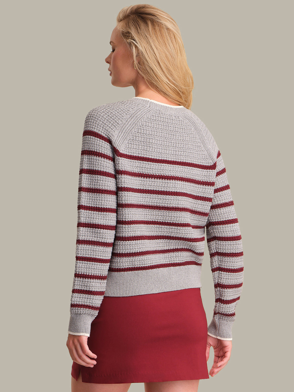 Woman wearing a gray sweater with red stripes and a red skirt on a plain background