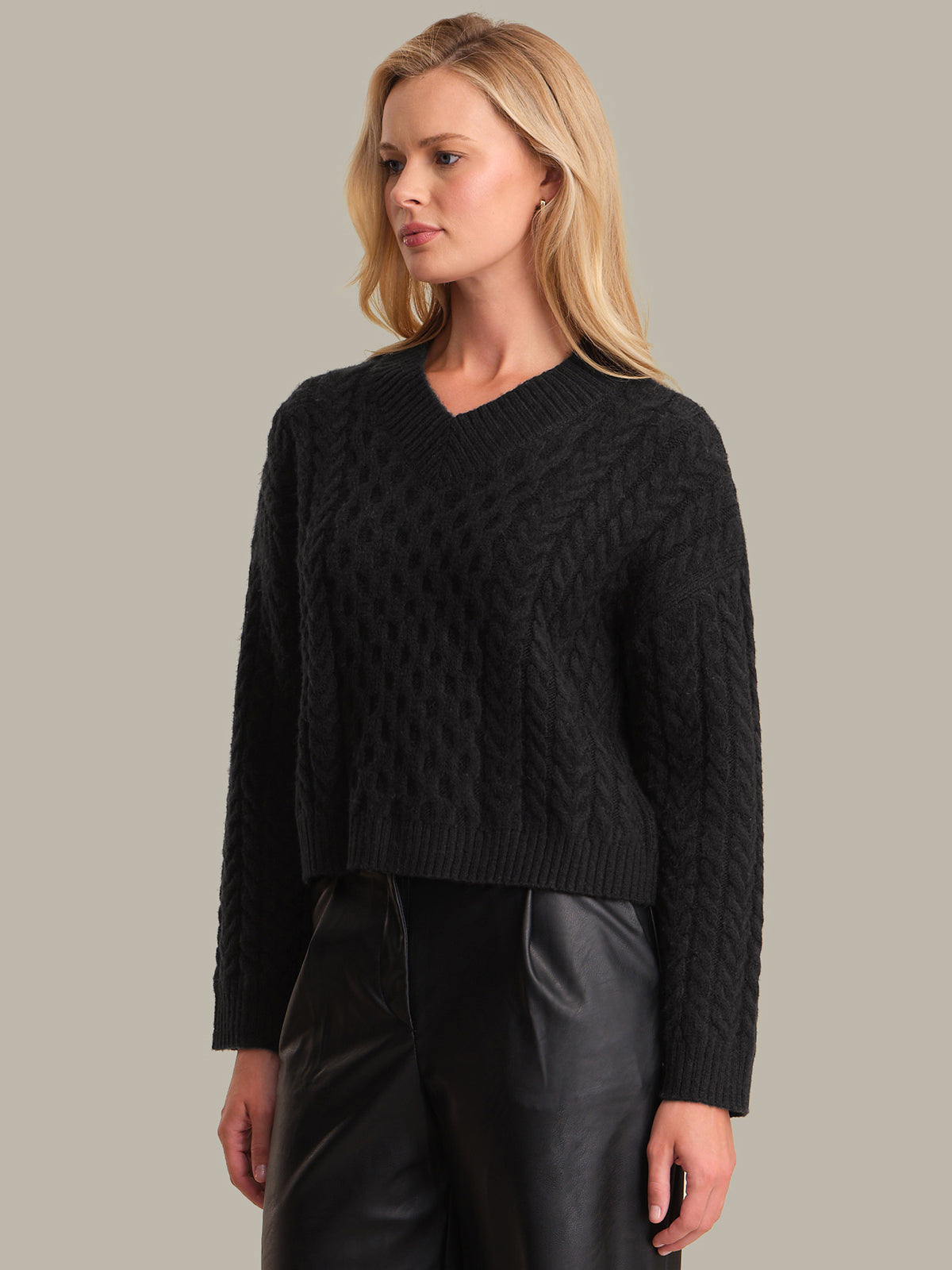 Woman wearing a black cable knit sweater against a neutral background