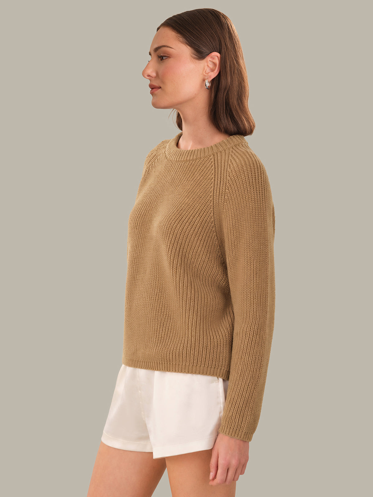 Woman wearing a brown ribbed sweater and white shorts on a gray background