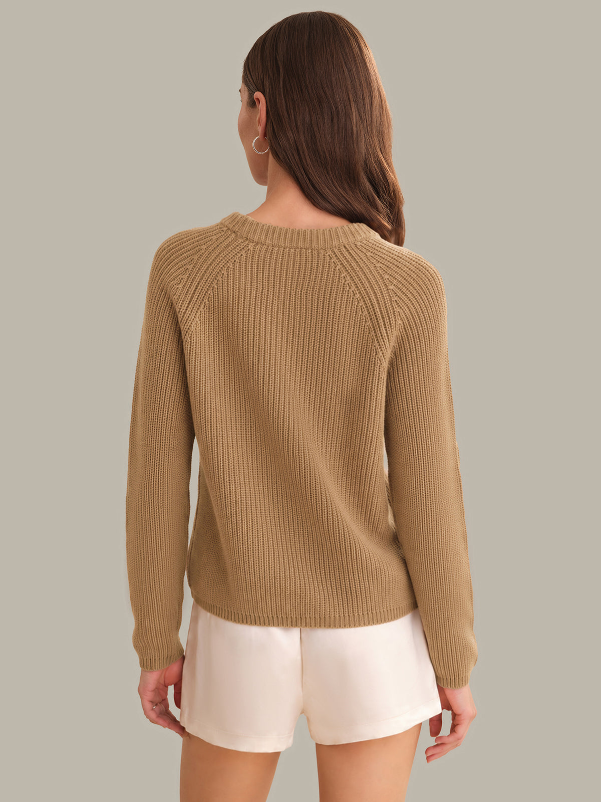 Woman wearing a brown sweater and white shorts on a plain background