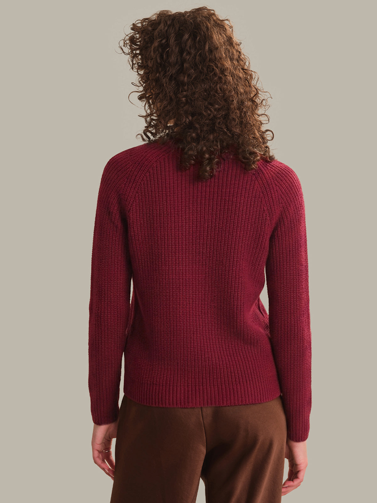 Person wearing a red sweater and brown pants against a plain background