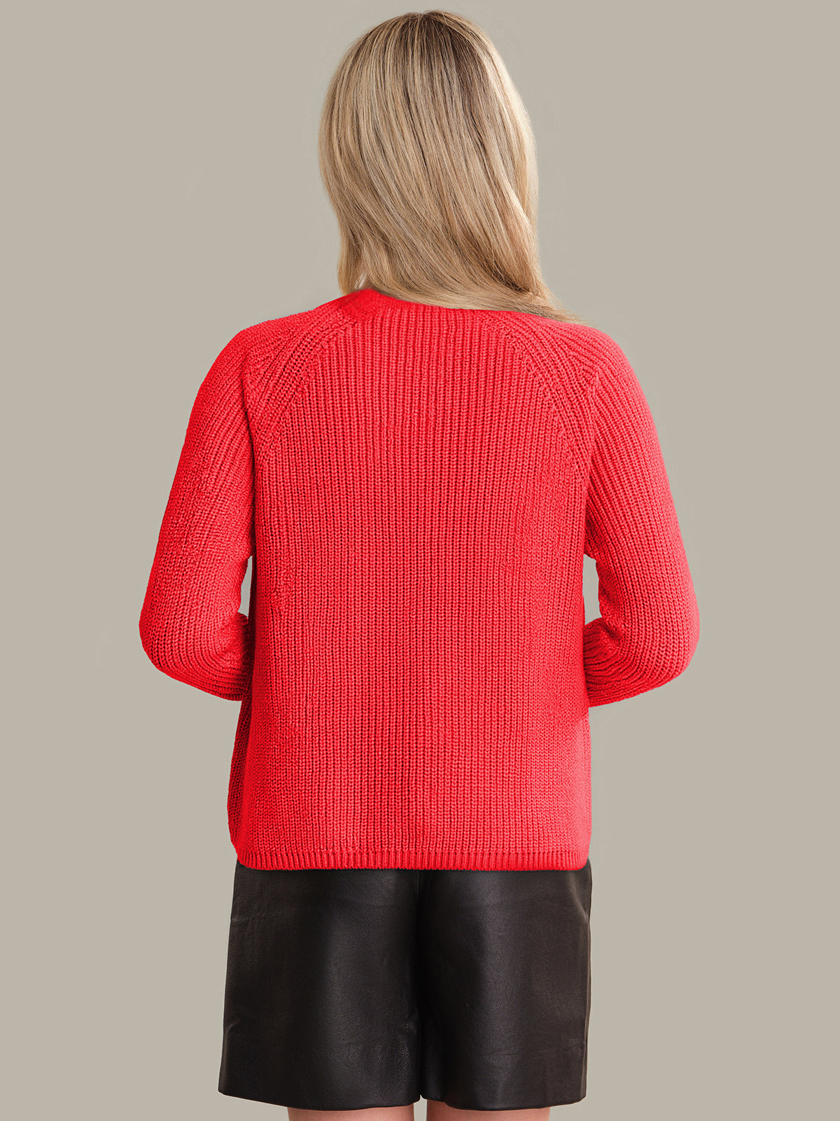 Person wearing a red sweater and black skirt on a beige background