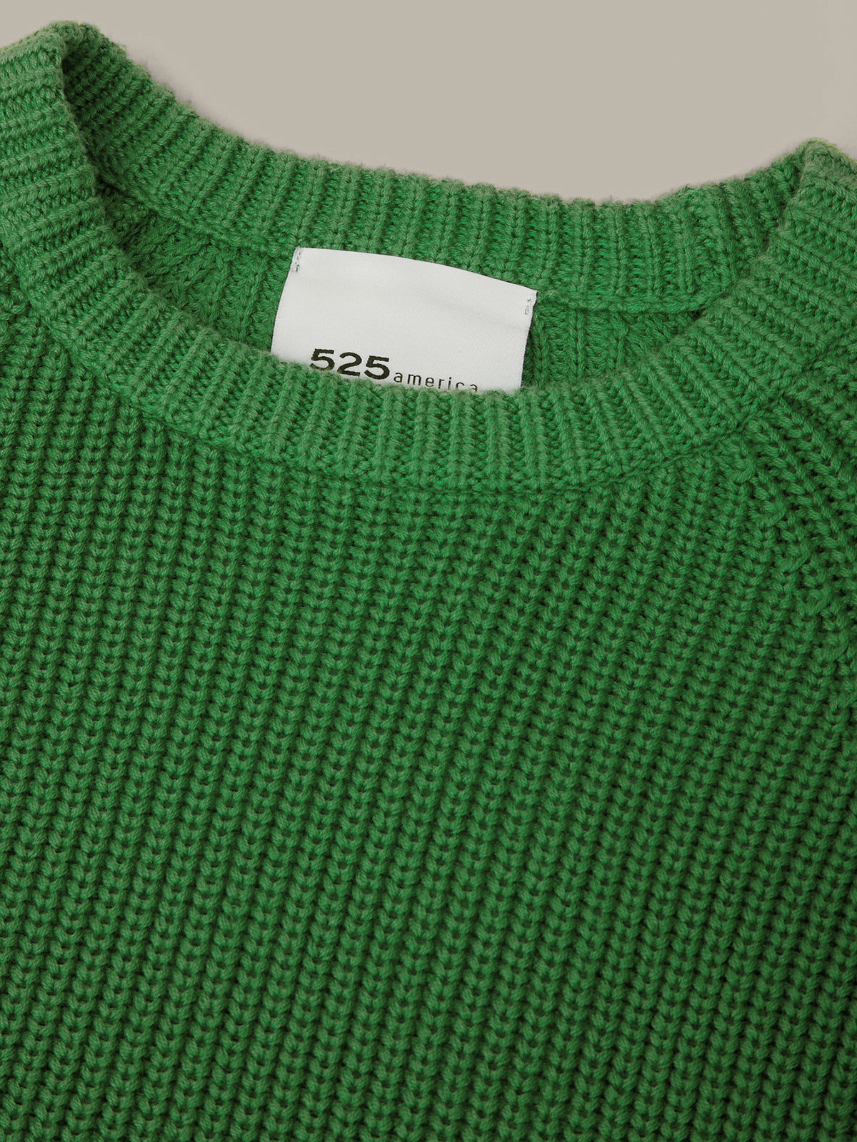 Close-up of a green sweater with a visible brand label on a neutral background
