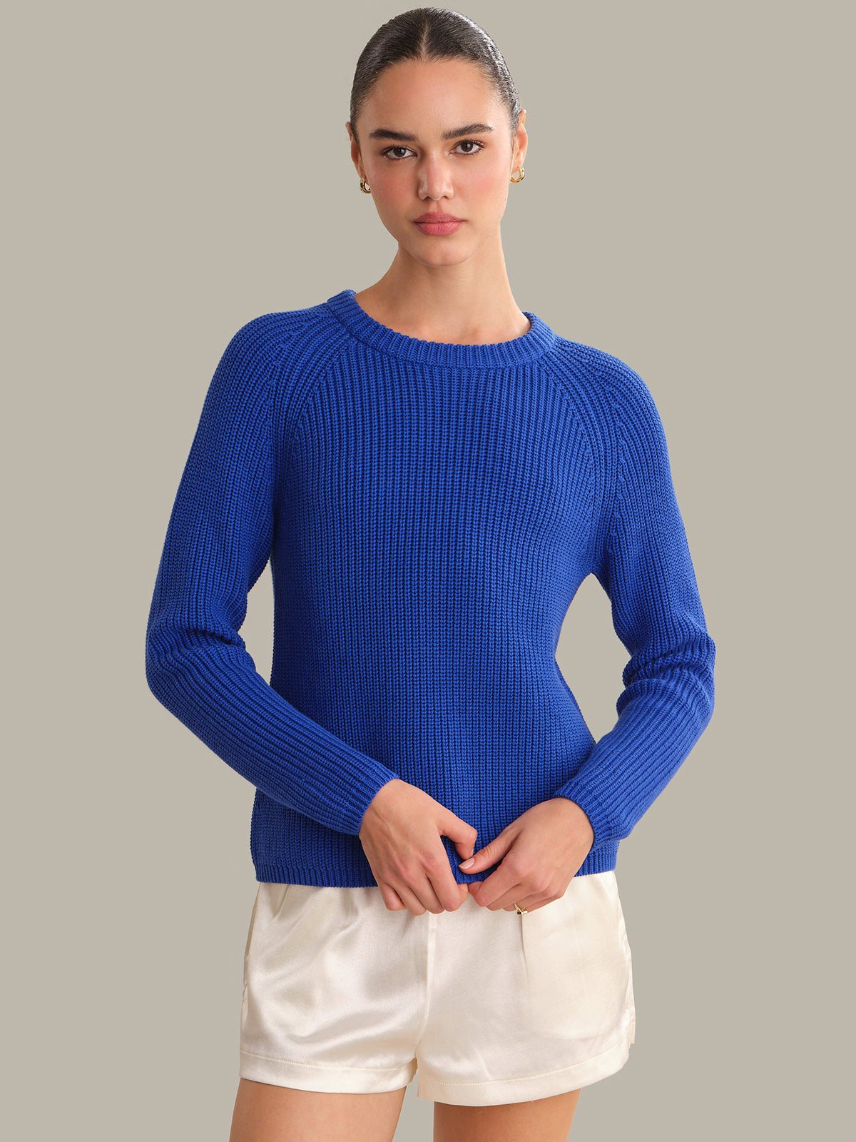 Person wearing a blue sweater and white shorts on a gray background