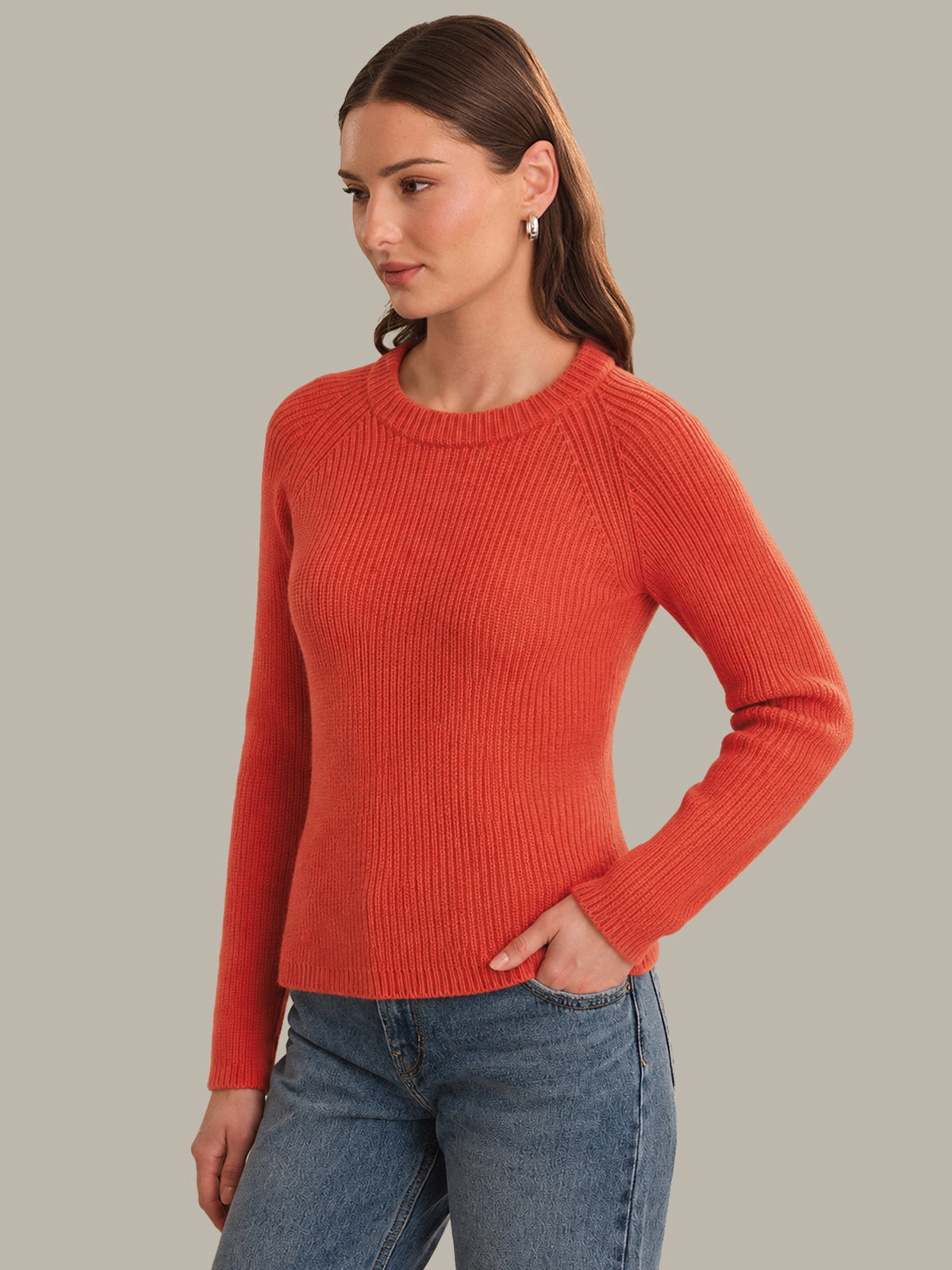 Woman wearing a red sweater and blue jeans against a gray background