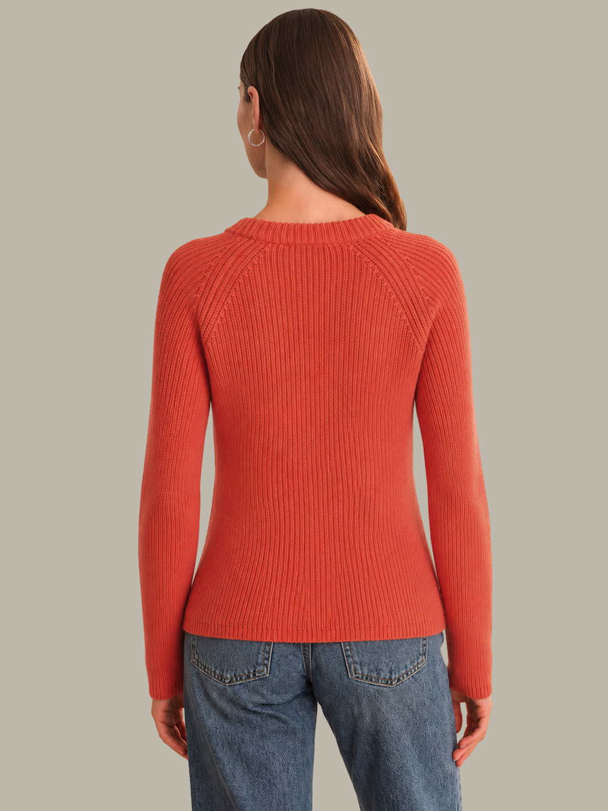 Person wearing a red sweater and blue jeans on a neutral background