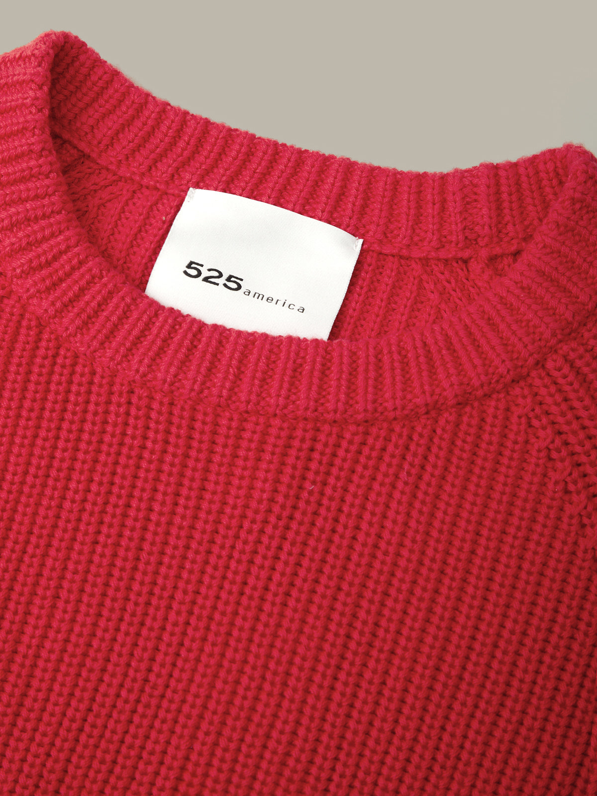 Close-up of a bright red ribbed knit sweater with a white neck label reading 525america, set against a plain light gray background.
