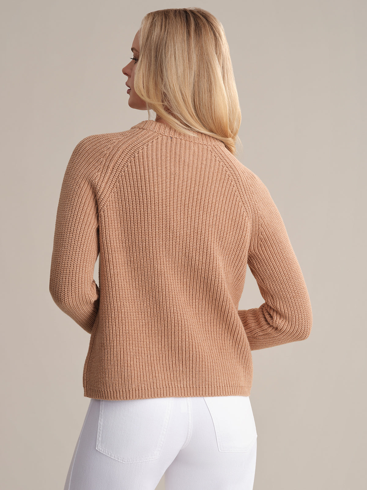 A person with long blonde hair wears the Jane: Crewneck Shaker Stitch Cotton Sweater in beige and white pants, facing away from the camera against a plain background.