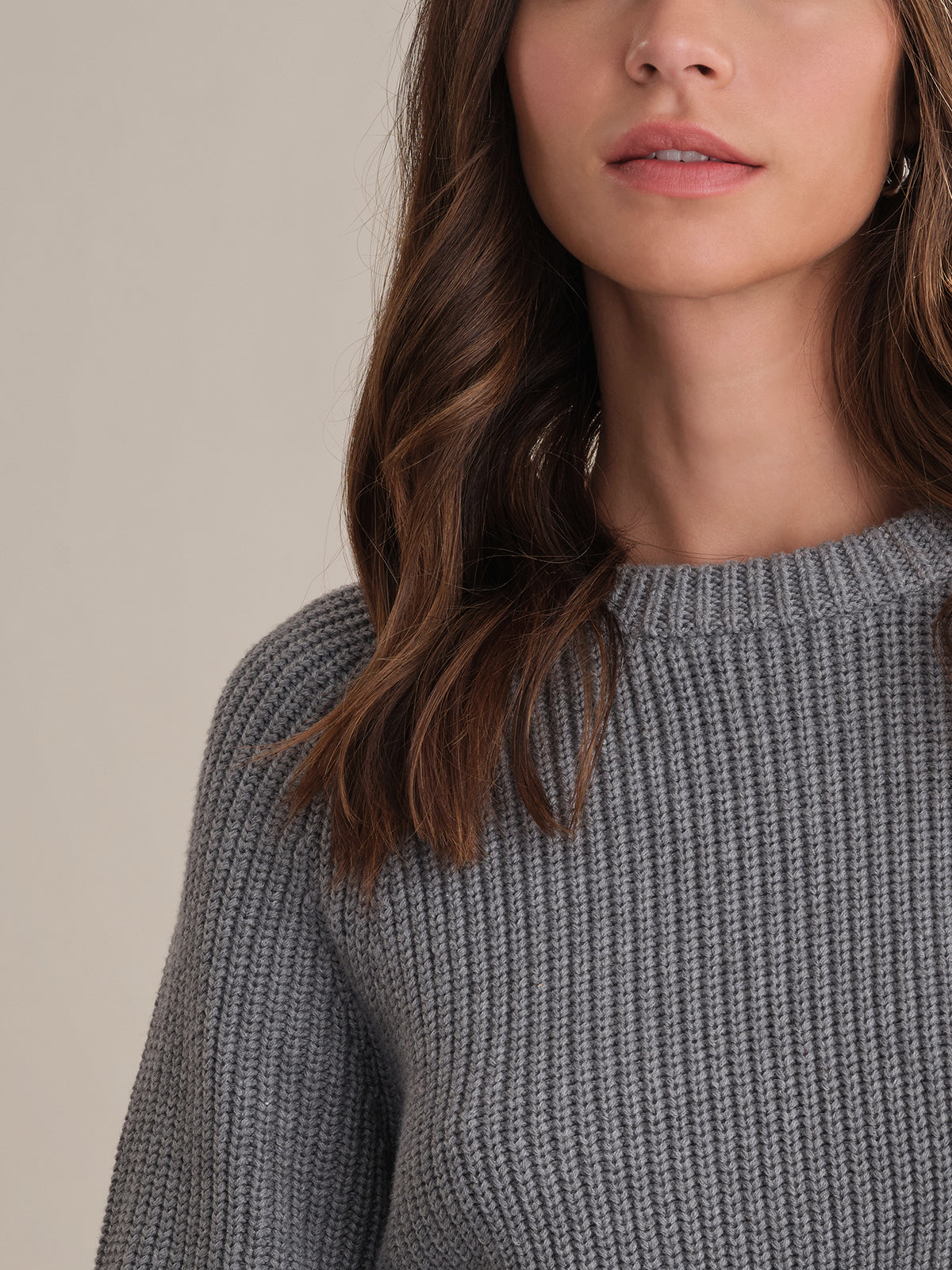 A woman with long brown hair wears a 525 America gray cotton shaker stitch sweater with a fitted silhouette. She is shown from the shoulders up, only the lower half of her face visible against a plain background.