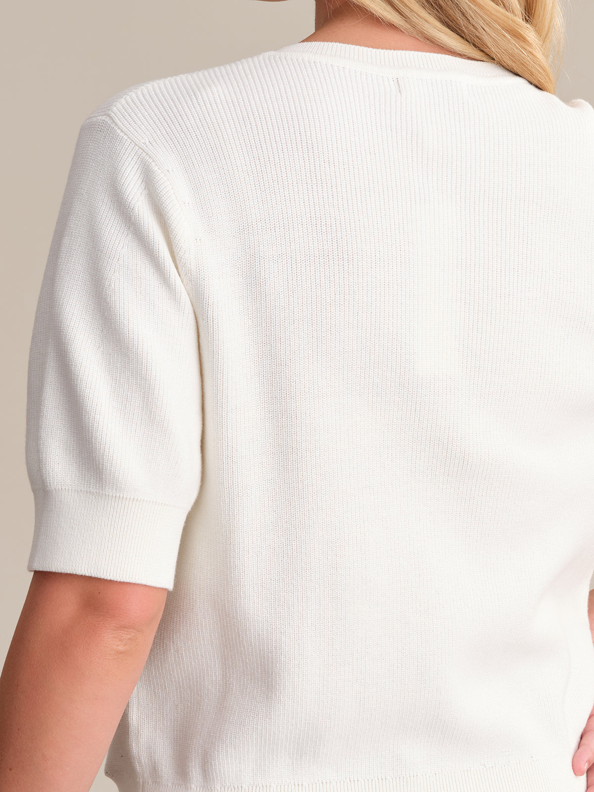 The image shows the back of a person wearing a white, short-sleeved rib-knit cotton sweater by 525 America. Their light hair cascades down their back, enhancing the relaxed silhouette.