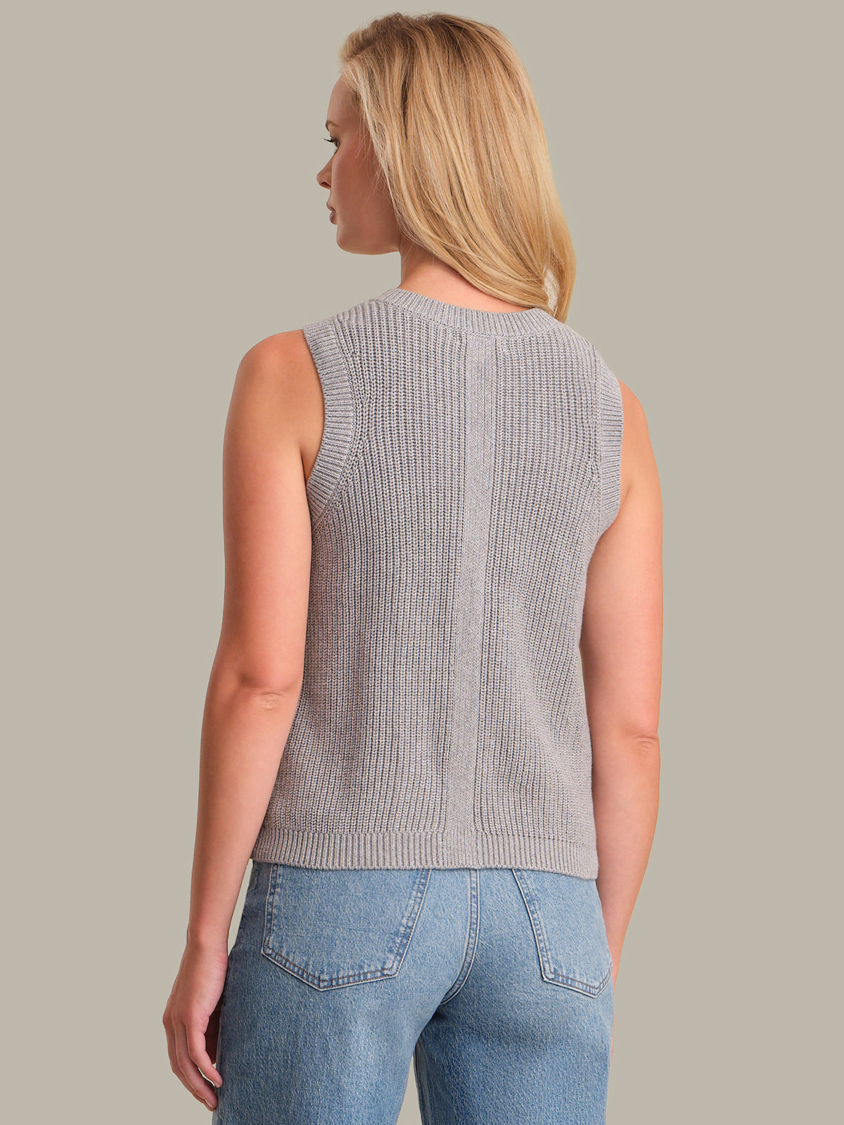 Woman wearing a gray sleeveless knitted top and blue jeans on a beige background