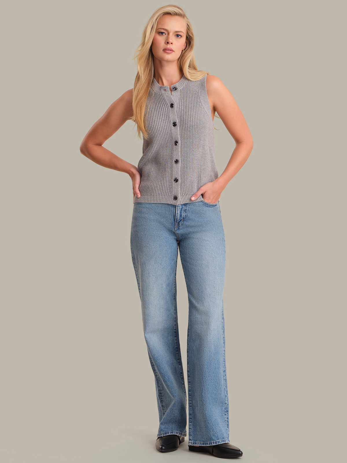 Woman wearing a sleeveless button-up top and blue jeans on a gray background