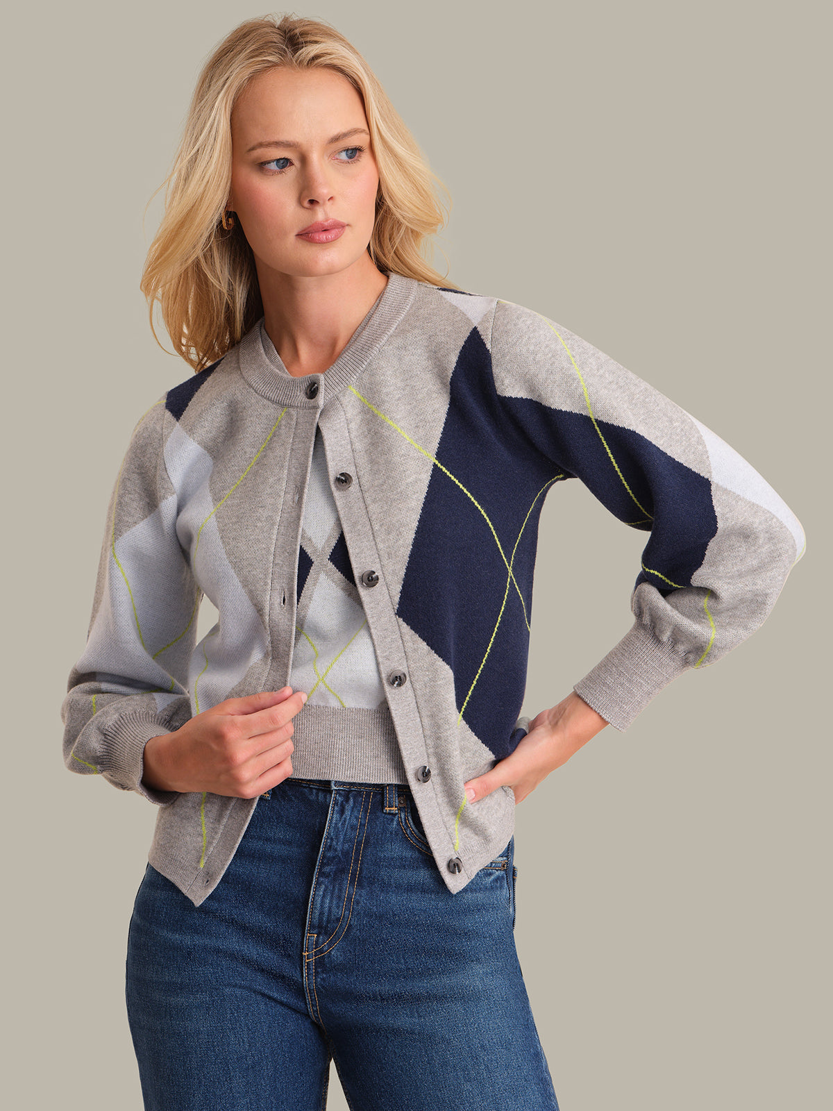 Woman wearing a patterned cardigan over a sweater and jeans on a plain background