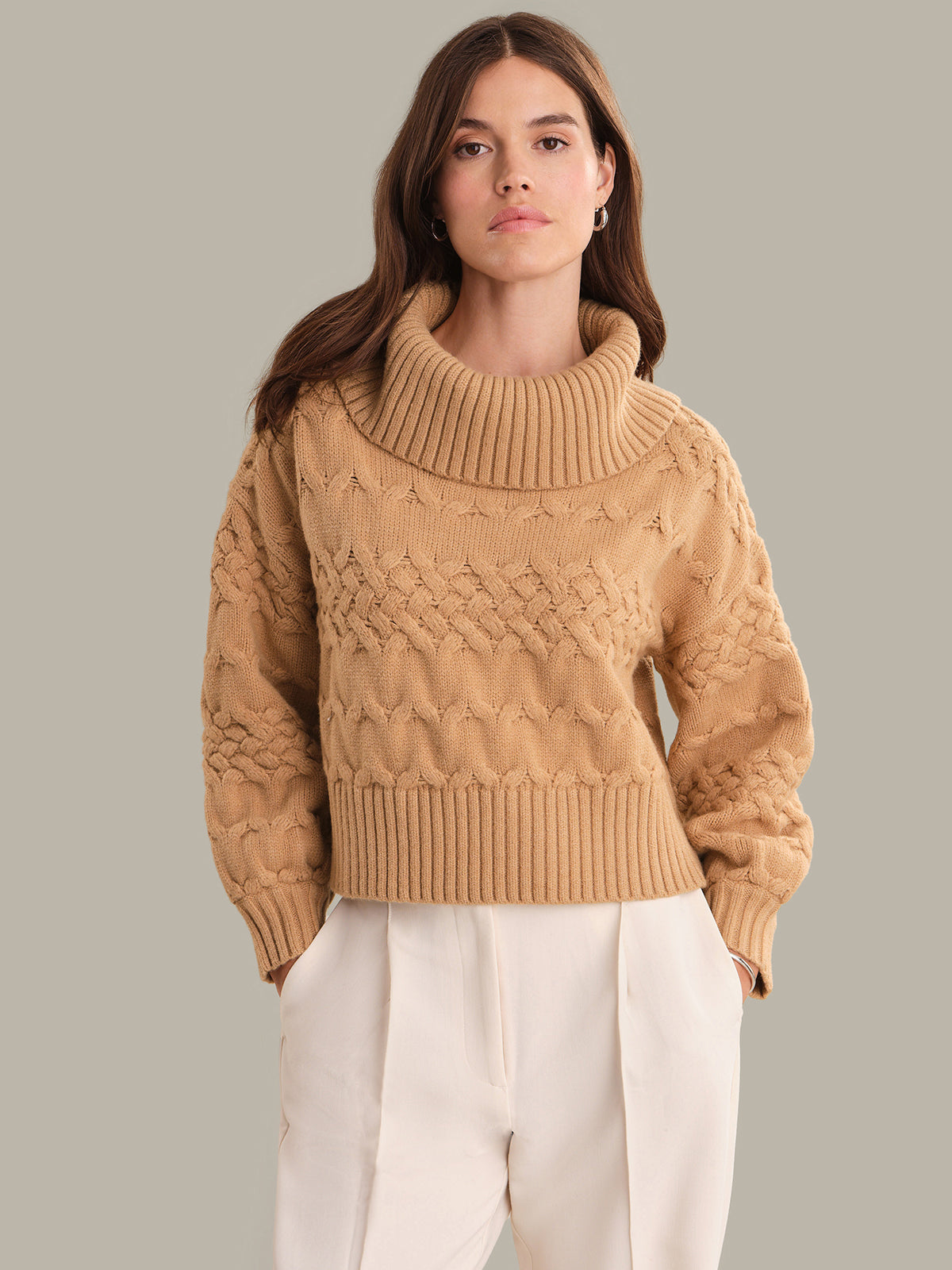 Woman wearing a beige cable knit sweater against a plain background