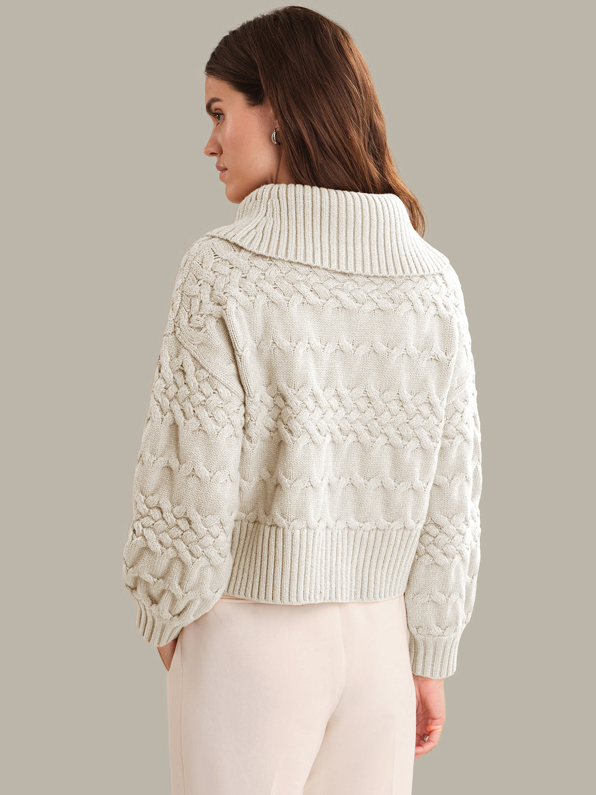 Woman wearing a cream cable knit sweater against a neutral background