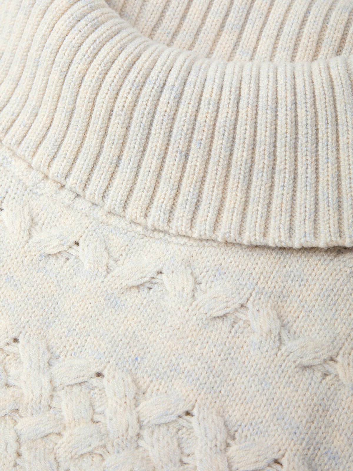 Close-up of a textured cream sweater with cable knit pattern