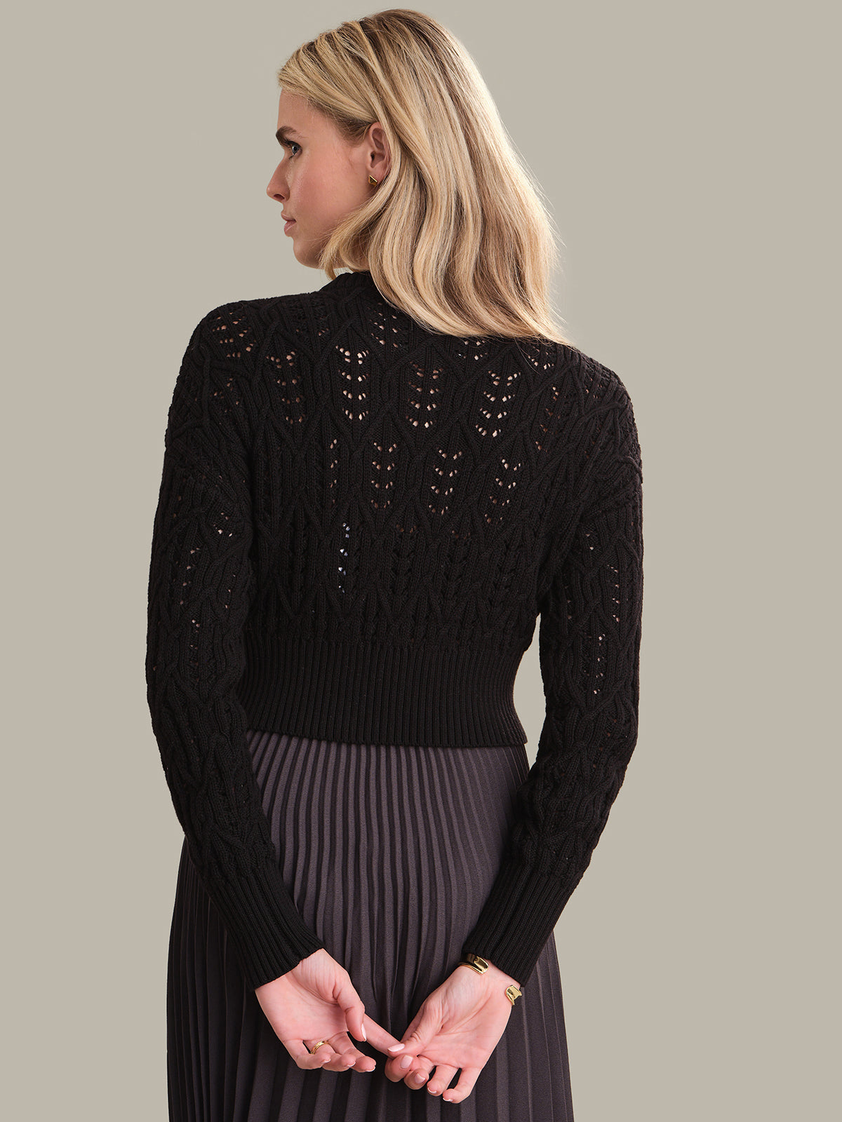 Woman wearing a black sweater with intricate back design on a neutral background