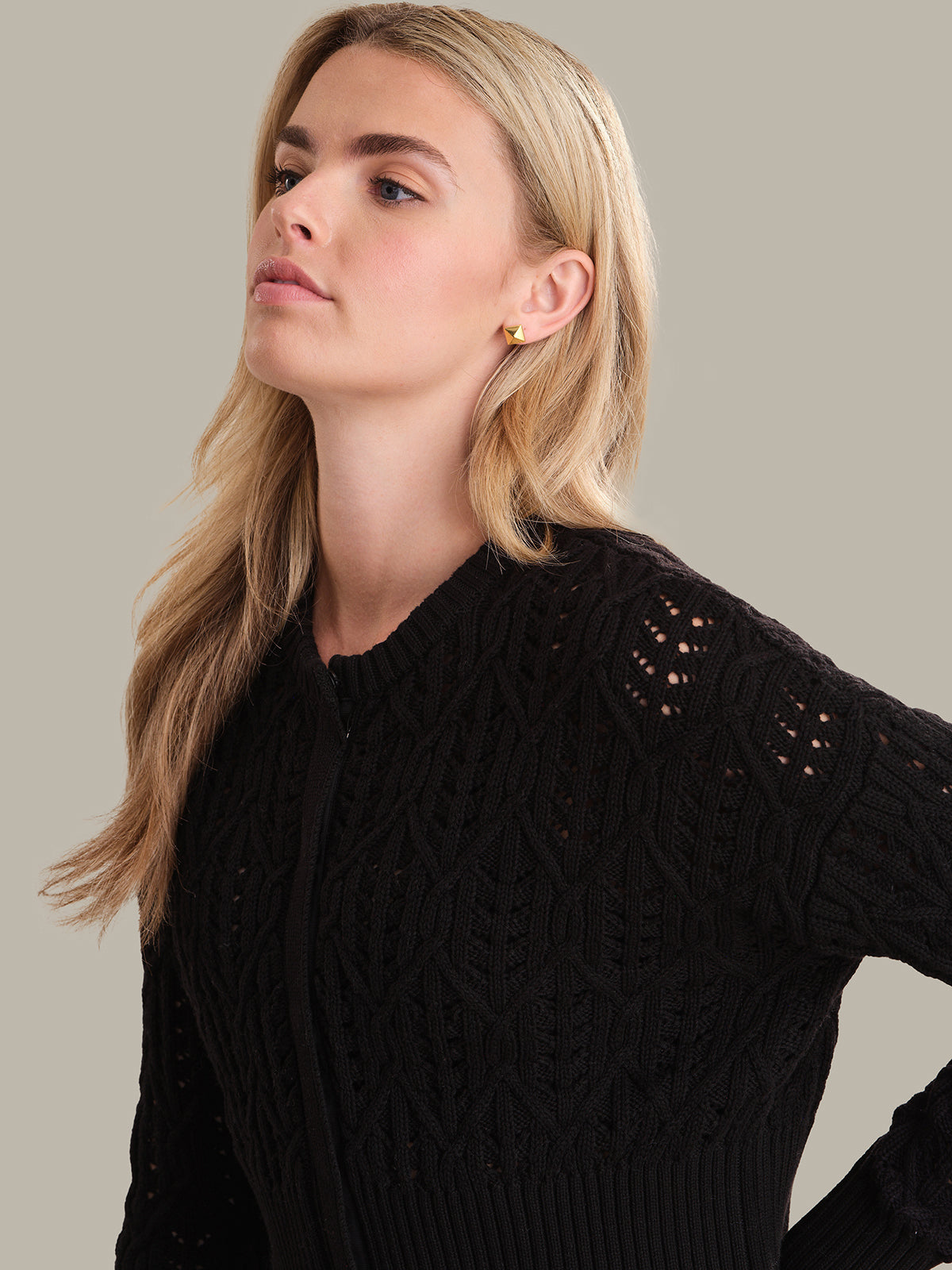Woman wearing a black cable knit sweater against a neutral background