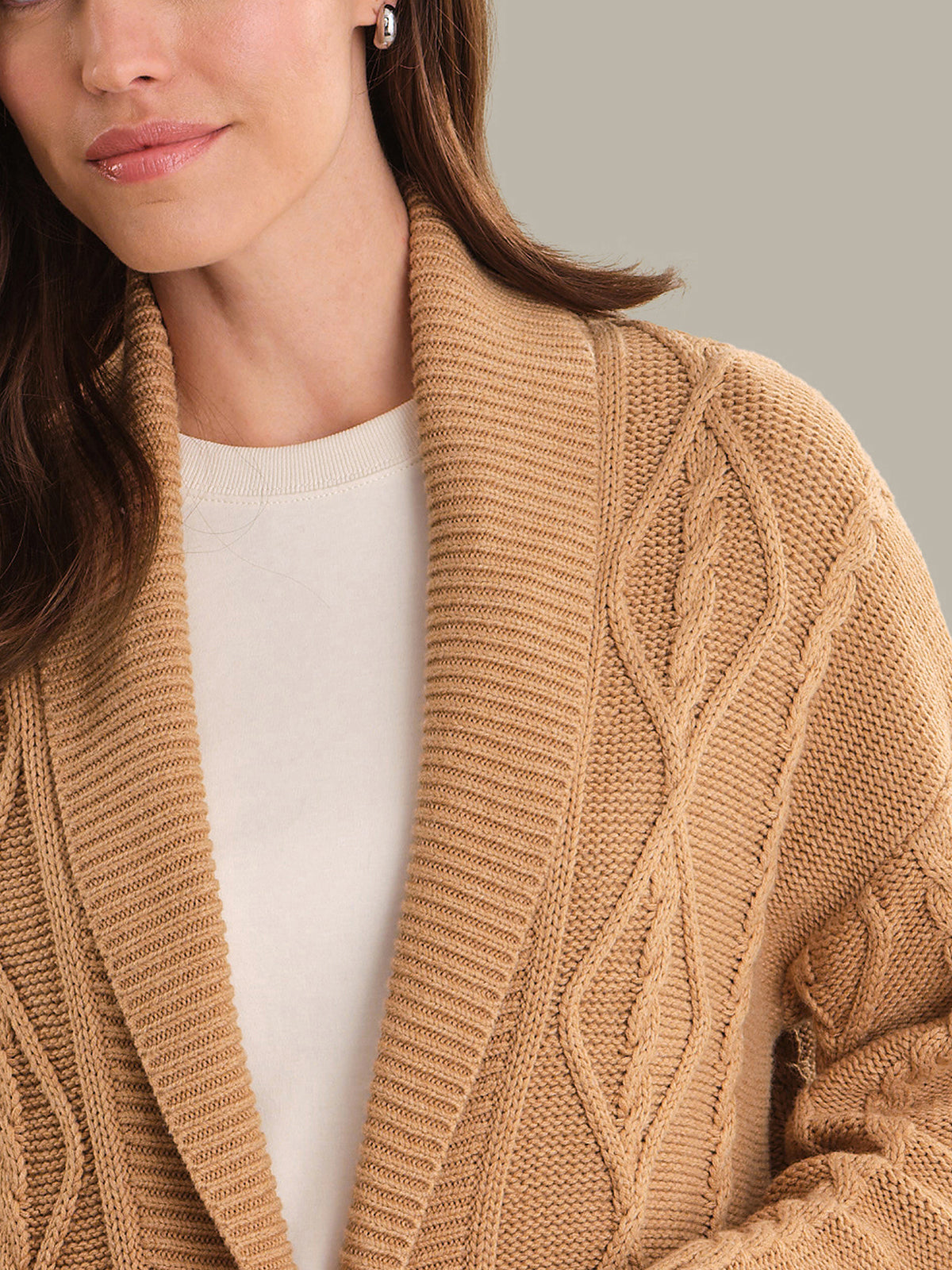 Close-up of a person wearing a brown cable knit cardigan over a white shirt.