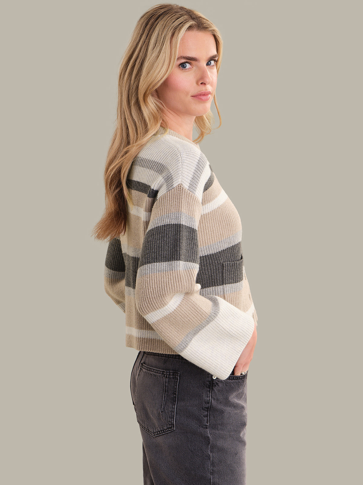 Woman wearing a striped sweater and dark jeans on a plain background