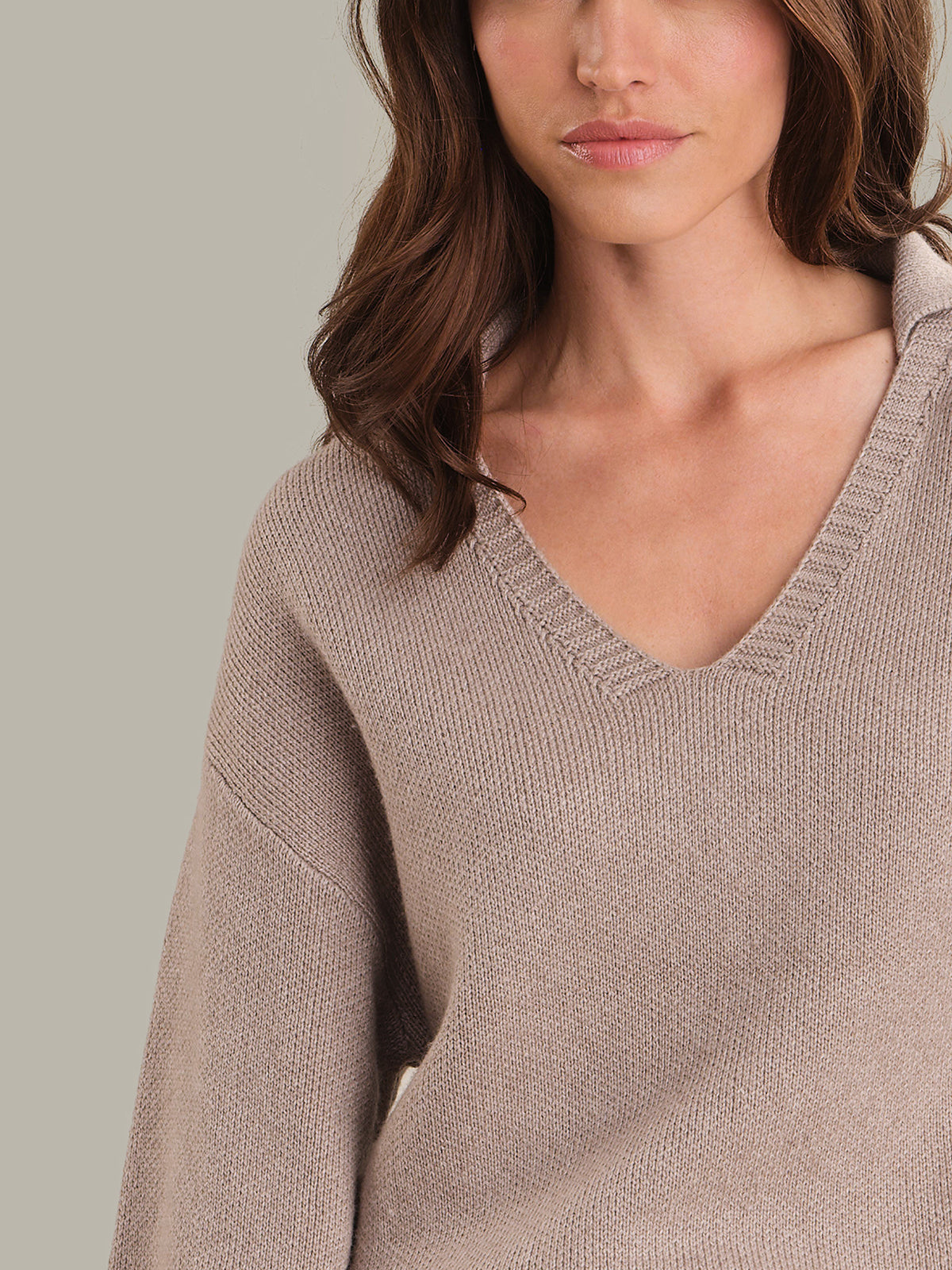 Close-up of a person wearing a beige sweater against a neutral background