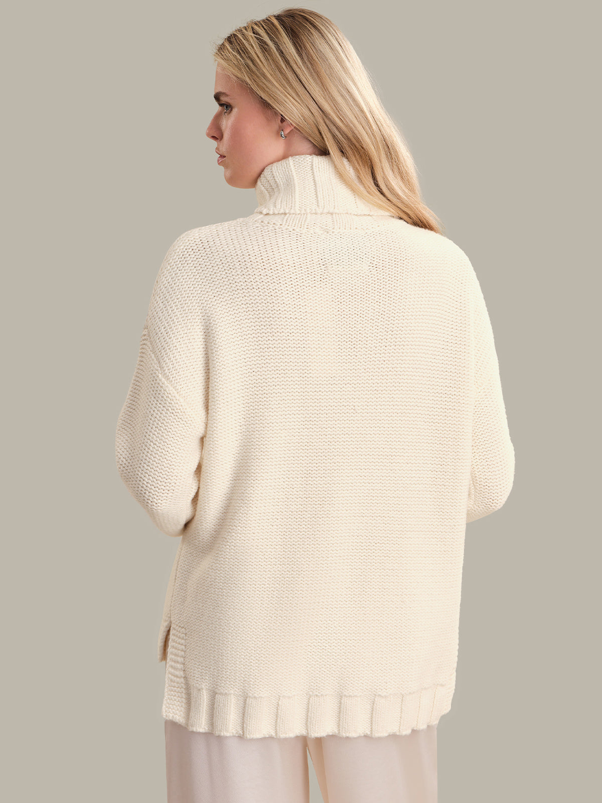 Woman wearing a cream-colored sweater against a plain background