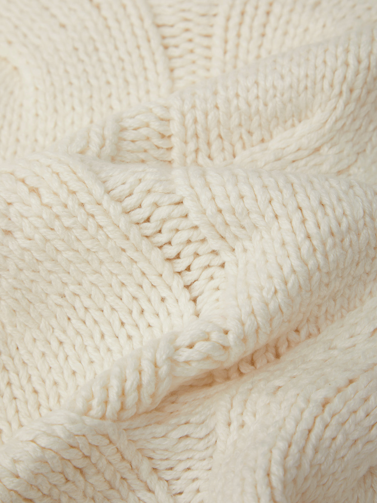 Close-up of a textured cream-colored fabric with a cable knit pattern.
