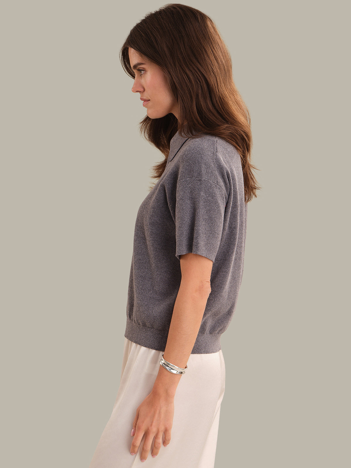Woman wearing a gray sweater and white pants against a plain background