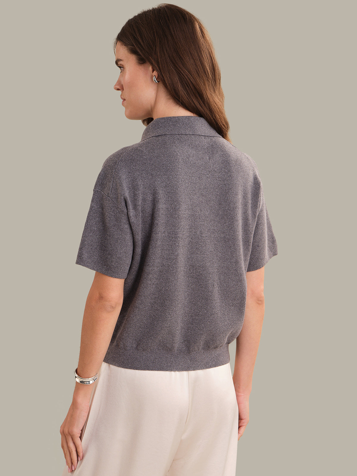 Woman wearing a gray polo shirt and white pants against a plain background