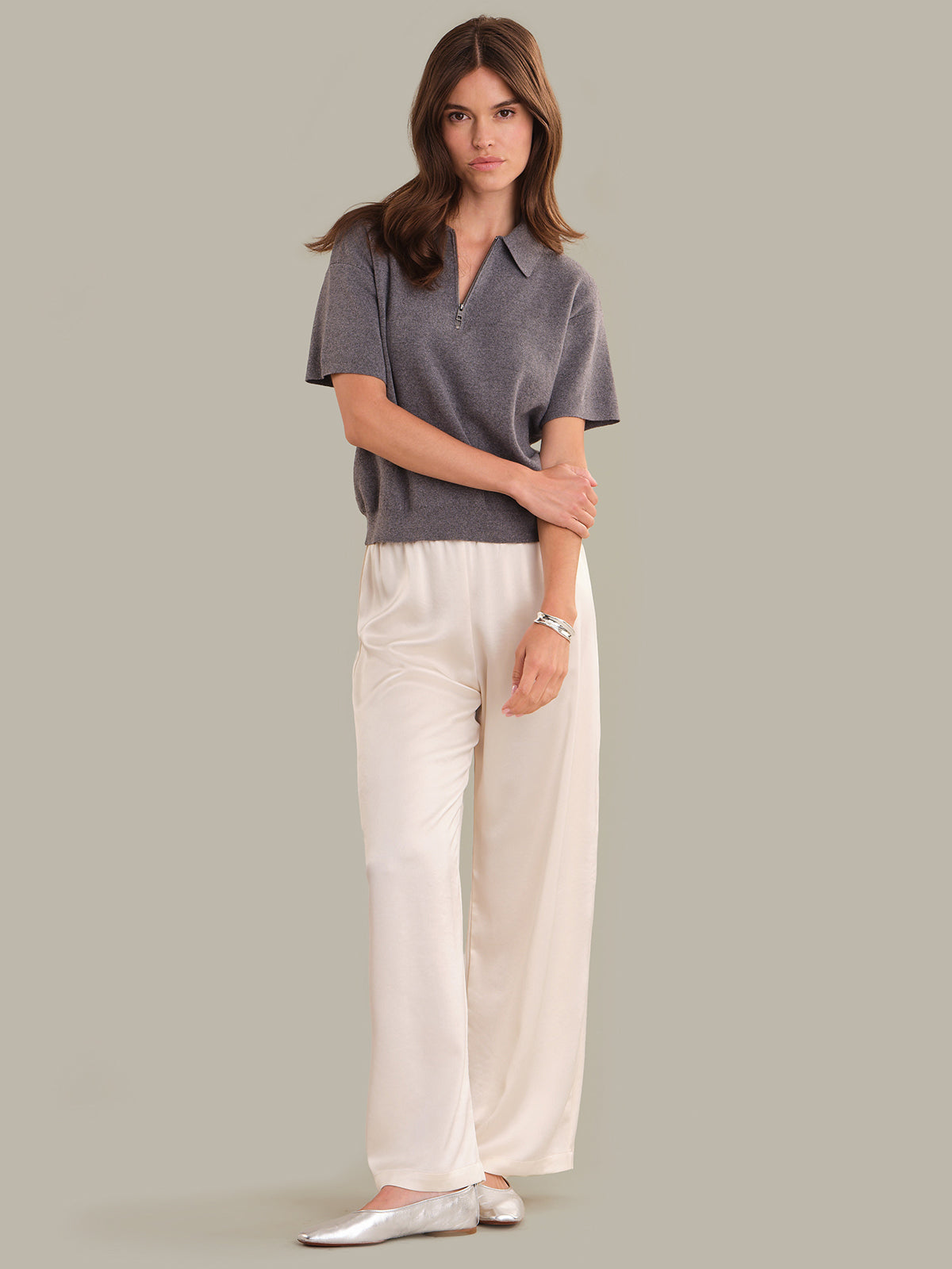 Woman wearing a gray polo shirt and white pants against a plain background