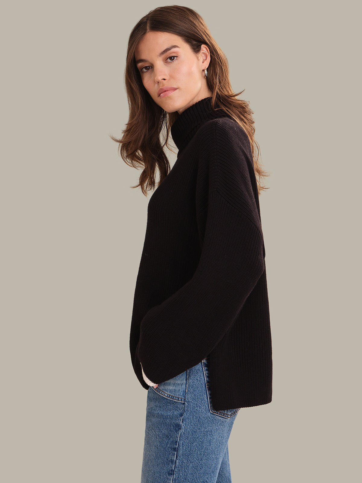 Woman wearing a black sweater and blue jeans on a gray background