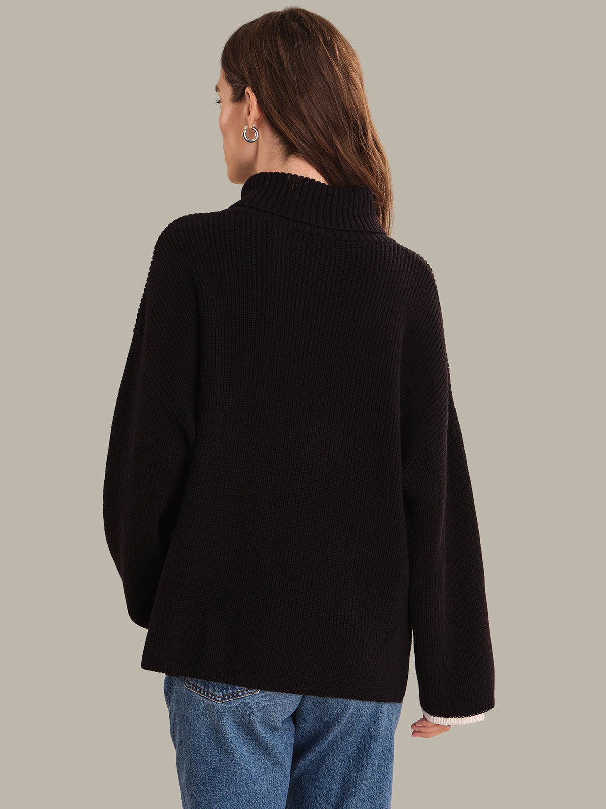 Person wearing a black sweater and blue jeans on a plain background